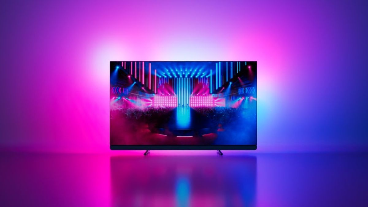 Ambilight TV von Philips mit 65 Zoll stark reduziert Ein Fernseher, der ein farbenfrohes Bild zeigt, strahlt per Hintergrundbeleuchtung eine Wand in Lila- und Rosa-Tönen an.