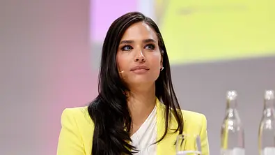 Amira Aly als Moderatorin mit offenen Haaren, ernster Mine und in einem gelben Blazer gekleidet.  - Foto: IMAGO / Panama Pictures