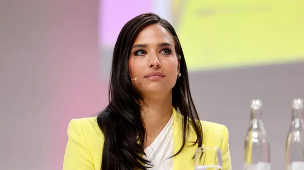 Amira Aly als Moderatorin mit offenen Haaren, ernster Mine und in einem gelben Blazer gekleidet.  - Foto: IMAGO / Panama Pictures