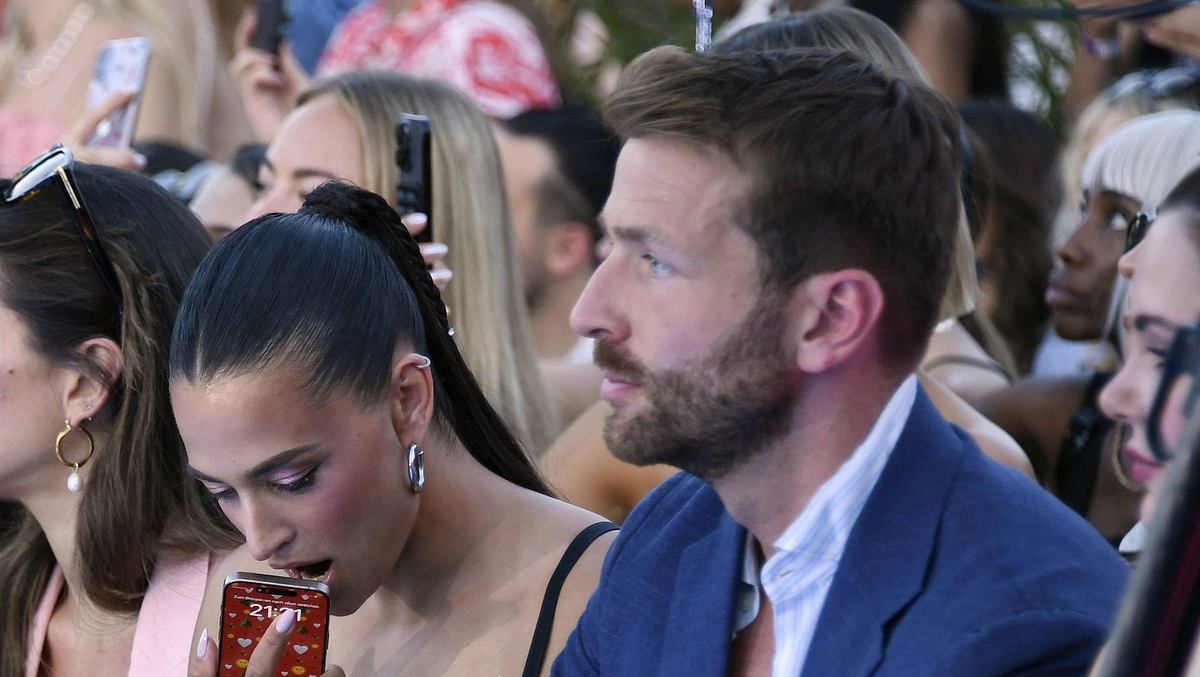 Amira Aly mit Freund Christian Düren auf der Berlin Fashion Week am 02.07.2025. Sie drückt ihr Handy gegen den offenen Mund, er schaut ernst.
