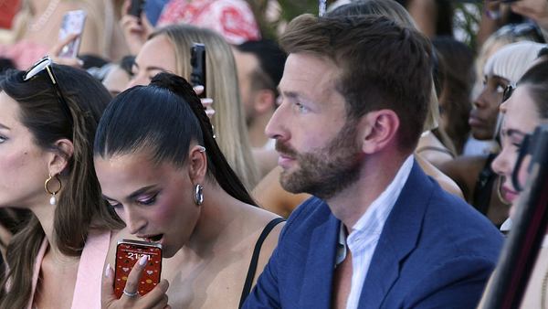 Amira Aly mit Freund Christian Düren auf der Berlin Fashion Week am 02.07.2025. Sie drückt ihr Handy gegen den offenen Mund, er schaut ernst. - Foto:  IMAGO / Marja