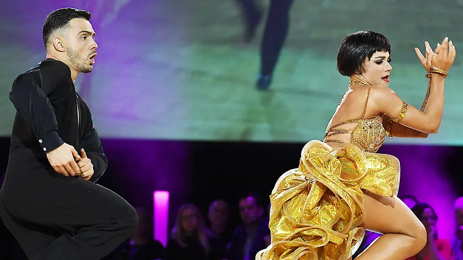 Anastasia und Sergiu Mărușter Tanzpaar Anastasia Stan und Sergiu Mărușter während eines Auftritts bei der EM 2023 in Leipzig. Sie trägt ein goldenes Kleid mit Rüschen, er einen dunklen Anzug. Beide befinden sich in einer kraftvollen Tanzpose