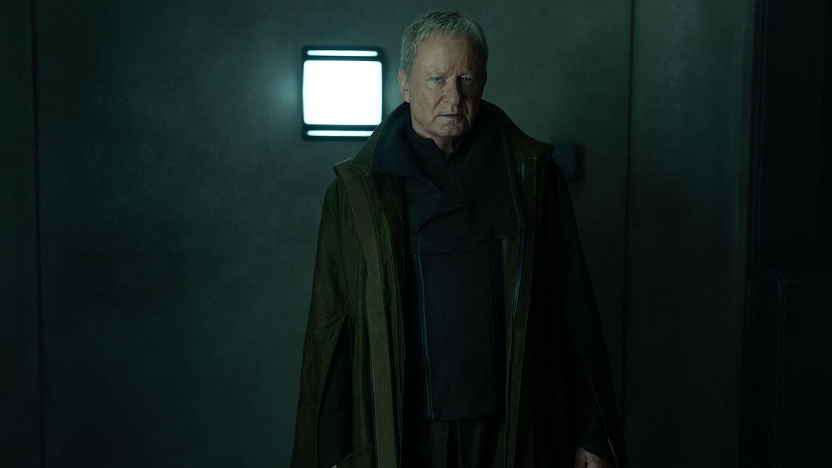 Luthen spielt eine entscheidende Rolle im Fall des Imperiums. Luthen schaut ernst nach vorne, an der Wand hinter ihm leuchtet eine Lampe.