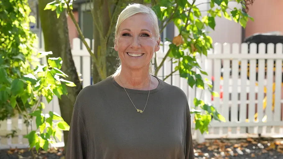 Andrea Kiewel Catch Us ProSieben Andrea Kiewel in einem dunkelgrauen Oberteil steht lächelnd vor einem Baum und einem weißen Lattenzaun.