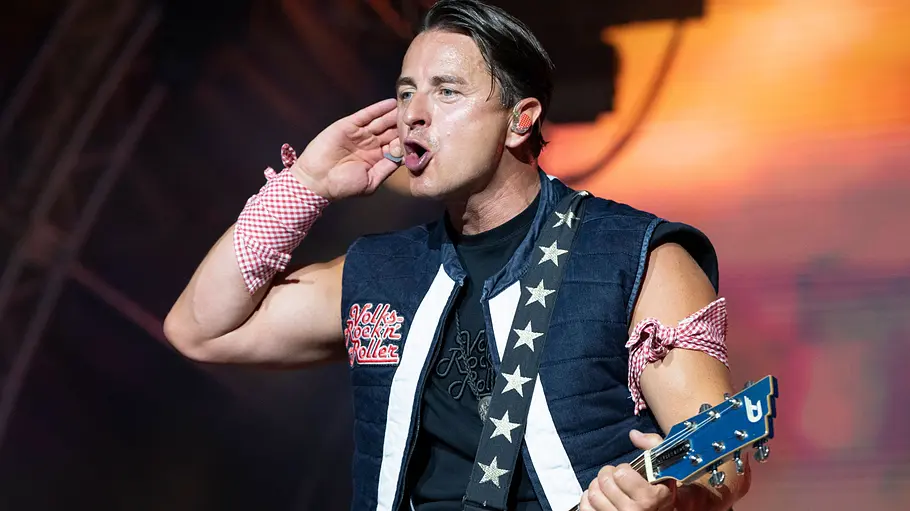 Andreas Gabalier Weihnachtsshow ZDF Andreas Gabalier steht mit blauer Gitarre und Headset-Mikrofon auf der Bühne und hält eine Hand ans Ohr.