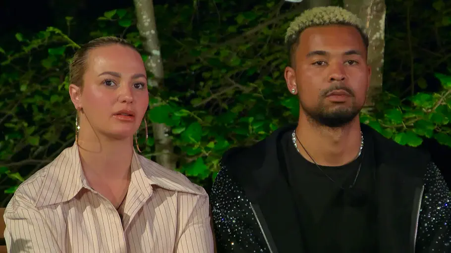 Anita Latifi und Fabrice Neda Anita Latifi im hellen Streifenhemd und Fabrice Neda in Schwarz sitzen nebeneinander vor Bäumen und grünem Laub.