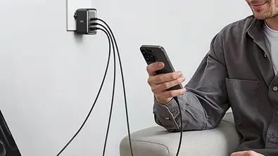 Ein Mehrfach-USB-C-Ladegerät von Anker steckt in einer Wandsteckdose und versorgt über drei Kabel mehrere Geräte. Eine Person sitzt auf einem Sofa und hält ein Smartphone, das mit dem Ladegerät verbunden ist. - Foto: Amazon/PR Ein Mehrfach-USB-C-Ladegerät von Anker steckt in einer Wandsteckdose und versorgt über drei Kabel mehrere Geräte. Eine Person sitzt auf einem Sofa und hält ein Smartphone, das mit dem Ladegerät verbunden ist. - Foto: Amazon/PR
