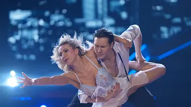 Anna-Carina im hellen Kostüm wird von Evgeny in einer dynamischen Hebefigur gehalten, im Hintergrund Lichterkulisse. - Foto: RTL / Stefan Gregorowius