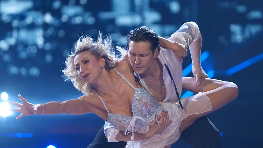 Anna-Carina Woitschack, Evgeny Vinokurov Anna-Carina im hellen Kostüm wird von Evgeny in einer dynamischen Hebefigur gehalten, im Hintergrund Lichterkulisse.