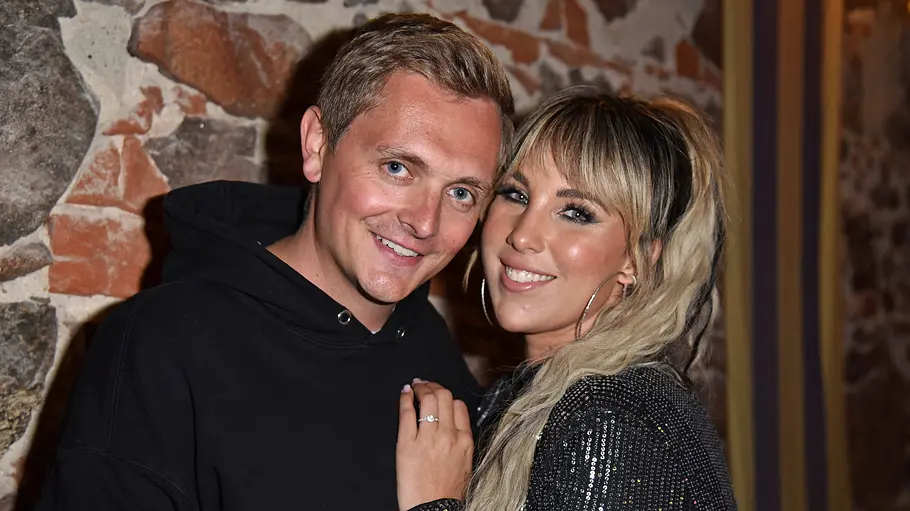 Annemarie Eilfeld und Tim Sandt Tim Sandt und Annemarie Eilfeld stehen eng beieinander vor einer Steinwand und lächeln. Sie trägt ein schwarzes Paillettenoberteil.