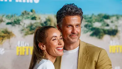 Annemarie lächelt im hellen Oberteil und Wayne schaut ernst im beigen Sakko. Beide posieren eng nebeneinander vor einer Fotowand. - Foto: IMAGO / Eventpress Annemarie lächelt im hellen Oberteil und Wayne schaut ernst im beigen Sakko. Beide posieren eng nebeneinander vor einer Fotowand. - Foto: IMAGO / Eventpress
