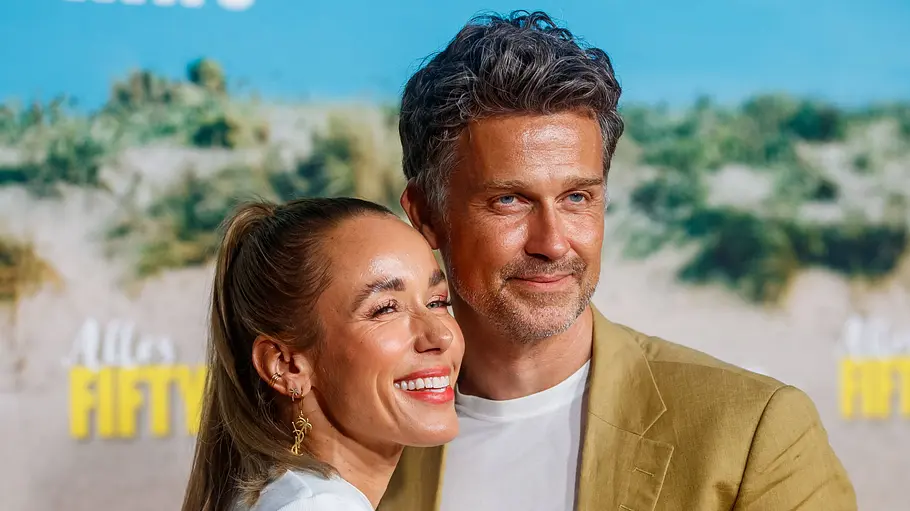 Annemarie und Wayne Carpendale sind auch nach der Trennung eng verbunden. Annemarie lächelt im hellen Oberteil und Wayne schaut ernst im beigen Sakko. Beide posieren eng nebeneinander vor einer Fotowand.