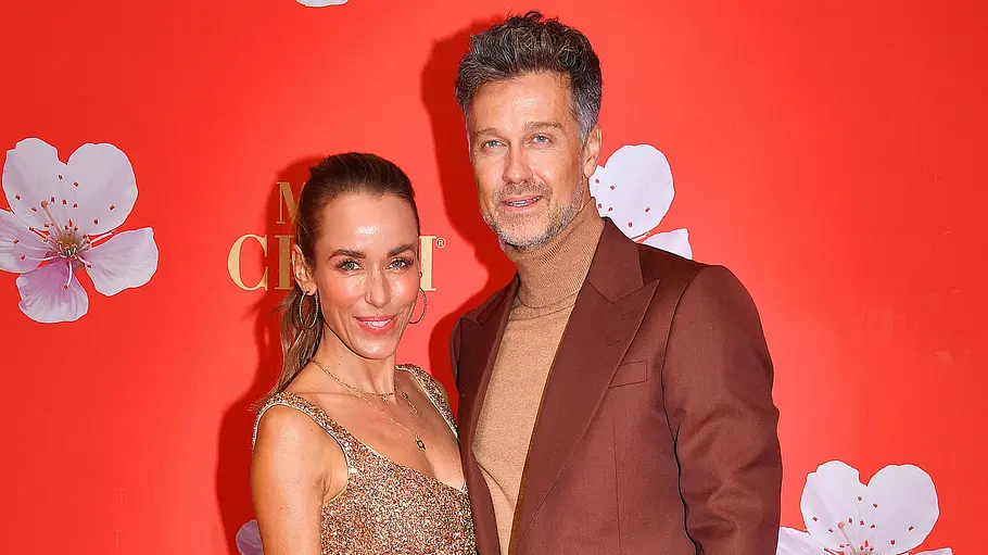 Annemarie und Wayne Carpendale bei einem gemeinsamen Auftritt Annemarie Carpendale steht in einem glitzernden Kleid neben Wayne Carpendale im braunen Anzug vor einer roten Fotowand.