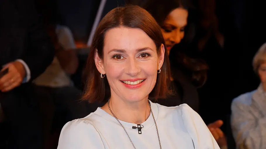 Schauspielerin Annett Renneberg trägt ein weißes Langarm-Oberteil und offene Haare, dabei lächelt sie in die Kamera.