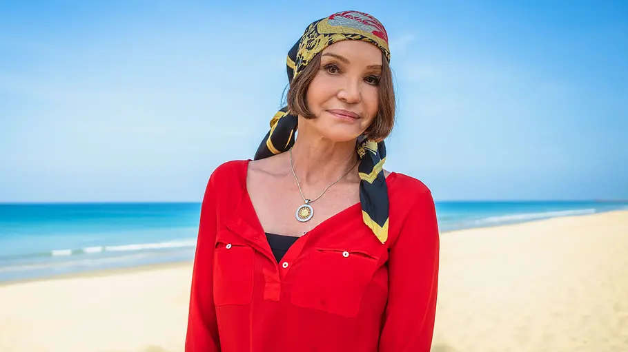 Anouschka Renzi ist Promi-Big-Brother-Kandidat 2026 Anouschka Renzi steht in roter Bluse und gemustertem Kopftuch an einem Sandstrand vor türkisblauem Meer.