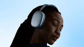 Frau trägt Apple AirPods Max 2 vor hellblauem Hintergrund - Foto: Apple