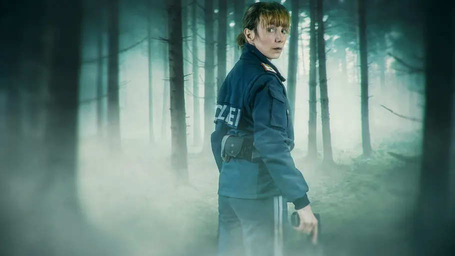ARD-Krimiserie „Das Vergessen - Spurlos im Moor“ Julia Koschitz steht als Polizistin Pia Kraus in dunkler Uniform in einem nebligen Wald und blickt über die Schulter zurück.