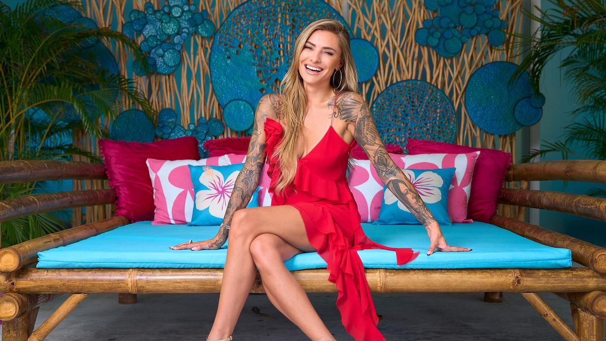 Sophia Thomalla posiert sitzend für AYTO in einem roten Kleid und lächelt