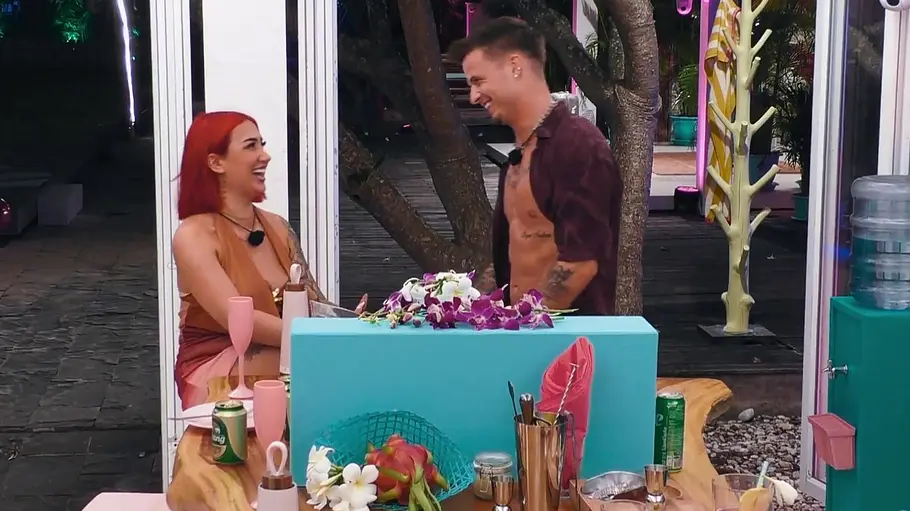 Francesca und Brian Francesca und Brian lachen einander an einer türkisfarbenen Bar mit Blumen, Getränken und Cocktailutensilien an.