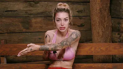 Ariel mit blondem Dutt und tätowiertem Arm sitzt im Dschungelcamp auf einer Holzbank und spricht emotional in die Kamera. - Foto: RTL