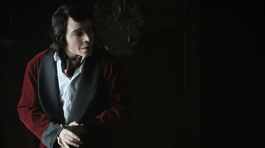Atlanta Teddy Perkins steht in einem dunklen Raum und trägt einen bordeauxroten Morgenmantel über einem weißen Hemd – eine Szene aus der Serie Atlanta.