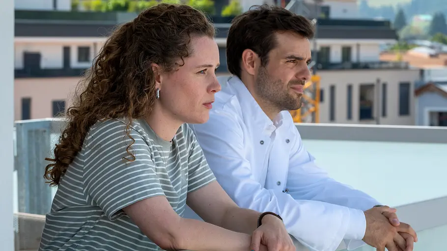 Auf der Dachterrasse der Klinik findet Dr. Jasper Graf (Lucas Reiber, r.) nach dem Verlust einer Patientin Trost bei Elli Kempfer (Klara Deutschmann, l.), die ihm beisteht. Einfach Elli - Verzeihen: Auf der Dachterrasse der Klinik unterhält sich Dr. Jasper Graf (Lucas Reiber) mit Elli Kempfer (Klara Deutschmann). Beide haben ihre Arme auf das Geländer gestützt. Beide machen einen besorgten Gesichtsausdruck.