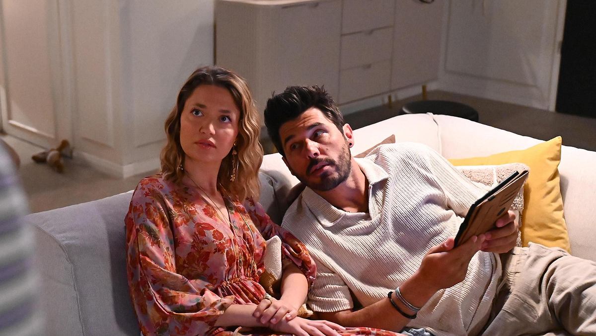 Nathalie und Matteo sitzen auf dem Sofa und schauen skeptisch nach oben.