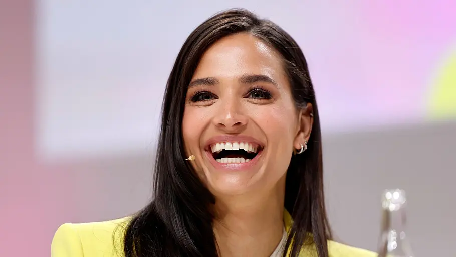 Babyname: Wie heißt Amira Alys Kind? Amira Aly, deren Tochter nun auf die Welt kam, lacht auf dem Foto mit offenem Mund. Sie trägt ein weißes Shirt und einen leuchtend gelben Blazer.