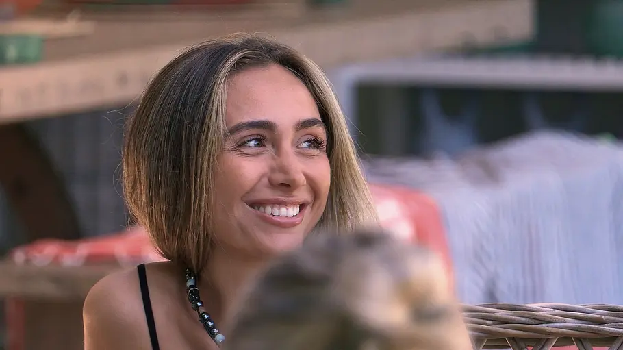 Nadja Bachelors-Nadja sitzt im Freien und blickt mit strahlendem Gesicht zu einer anderen Person außerhalb des Bildes.
