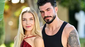 Reality-TV-Paar Michelle und Maki posiert eng umschlungen im Freien. Michelle trägt ein bordeauxrotes Kleid, Maki ein schwarzes Tanktop und helle Hose. Beide blicken lächelnd in die Kamera, während im Hintergrund Palmen und üppige Vegetation zu sehen sind. - Foto: RTL / Markus Hertrich Reality-TV-Paar Michelle und Maki posiert eng umschlungen im Freien. Michelle trägt ein bordeauxrotes Kleid, Maki ein schwarzes Tanktop und helle Hose. Beide blicken lächelnd in die Kamera, während im Hintergrund Palmen und üppige Vegetation zu sehen sind. - Foto: RTL / Markus Hertrich