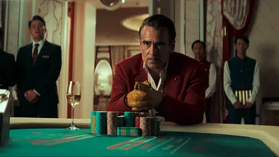 Colin Farrell sitzt in einem dunkelroten Anzug an einem Spieltisch. - Foto: Netflix
