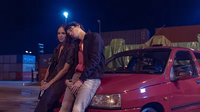 Zoe Fürmann (l.) und Eren M. Güvercin lehnen an einem roten Auto.  - Foto: HBO Max/Anne Wilk