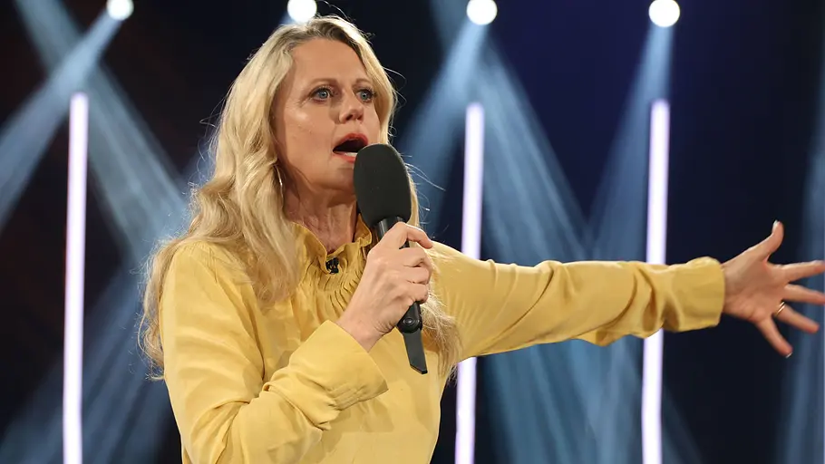 Barbara Schöneberger wurde im Netz beleidigt. Barbara Schöneberger trägt eine gelbe Bluse und spricht in ein Mikro