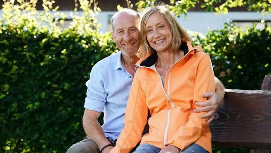 Hans und Elke aus „Bauer sucht Frau“ sitzen eng nebeneinander auf einer Bank im Grünen und lächeln in die Kamera.