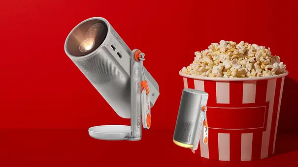 Ein Mini Beamer vor rotem Hintergrund, daneben ein Eimer Popcorn - Foto: Amazon/PR/Canva Ein Mini Beamer vor rotem Hintergrund, daneben ein Eimer Popcorn - Foto: Amazon/PR/Canva