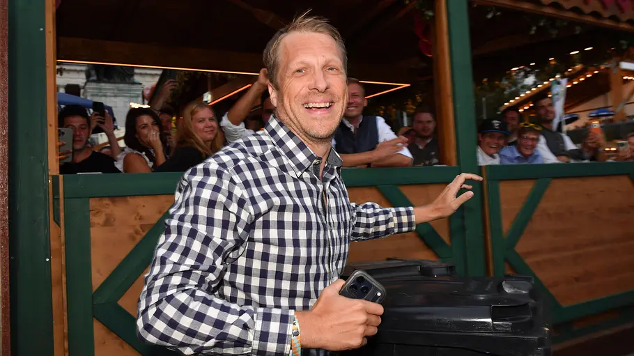 Bei diesem Angebot war selbst Oliver Pocher kurz ganz kleinlaut. Oliver Pocher lächelt im karierten Hemd mit einem Smartphone in der Hand. Hinter einer Holzbrüstung stehen mehrere Menschen.