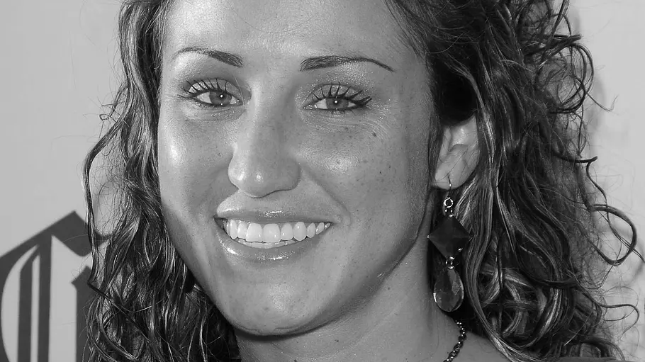 Big Brother-Teilnehmerin Amber Siyavus tot Amber Siyavus lächelt auf einem Schwarz-Weiß-Porträt. Sie trägt lockiges Haar, lange Ohrringe und eine Kette mit großem Anhänger.
