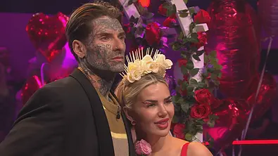 Nikola und Kim Virginia mit Blumenkrone stehen eng beieinander vor roten Rosen und Herzballons. - Foto: Joyn Nikola und Kim Virginia mit Blumenkrone stehen eng beieinander vor roten Rosen und Herzballons. - Foto: Joyn