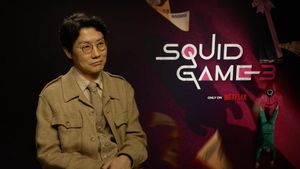 Dong-Hyuk vor dem „Squid Game“-Logo mit einem sanften Lächeln im Gesicht - Foto: Netflix