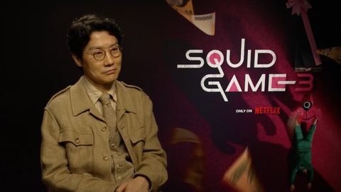 Dong-Hyuk vor dem „Squid Game“-Logo mit einem sanften Lächeln im Gesicht - Foto: Netflix