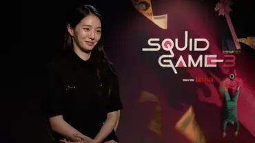 Park Gyu-young sitzt vor einem „Squid Game“-Poster und lächelt. - Foto: Netflix Park Gyu-young sitzt vor einem „Squid Game“-Poster und lächelt. - Foto: Netflix