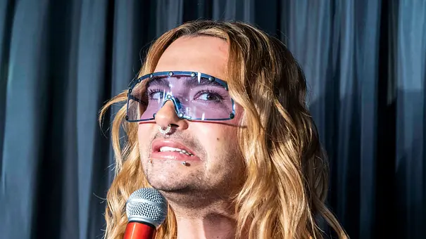 Bill Kaulitz trägt eine blau getönte Sonnenbrille und offene Haare. Er zieht die Mundwinkel nach unten. - Foto: IMAGO / BREUEL-BILD