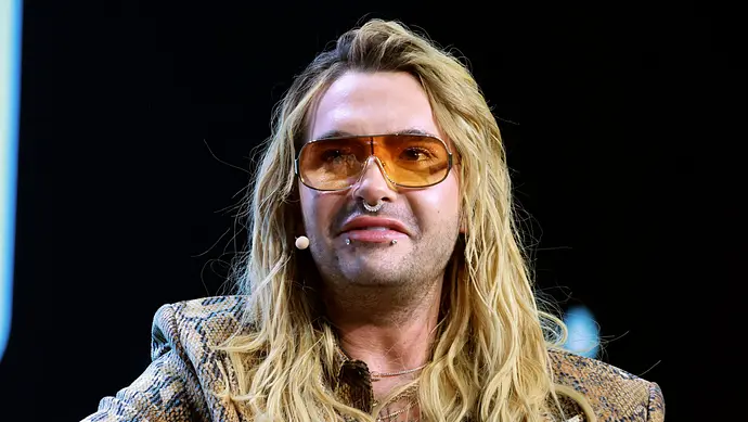 Bill Kaulitz trägt offene Haare und eine leicht getönte Sonnenbrille. Er sieht fassungslos aus. - Foto: IMAGO / Future Image