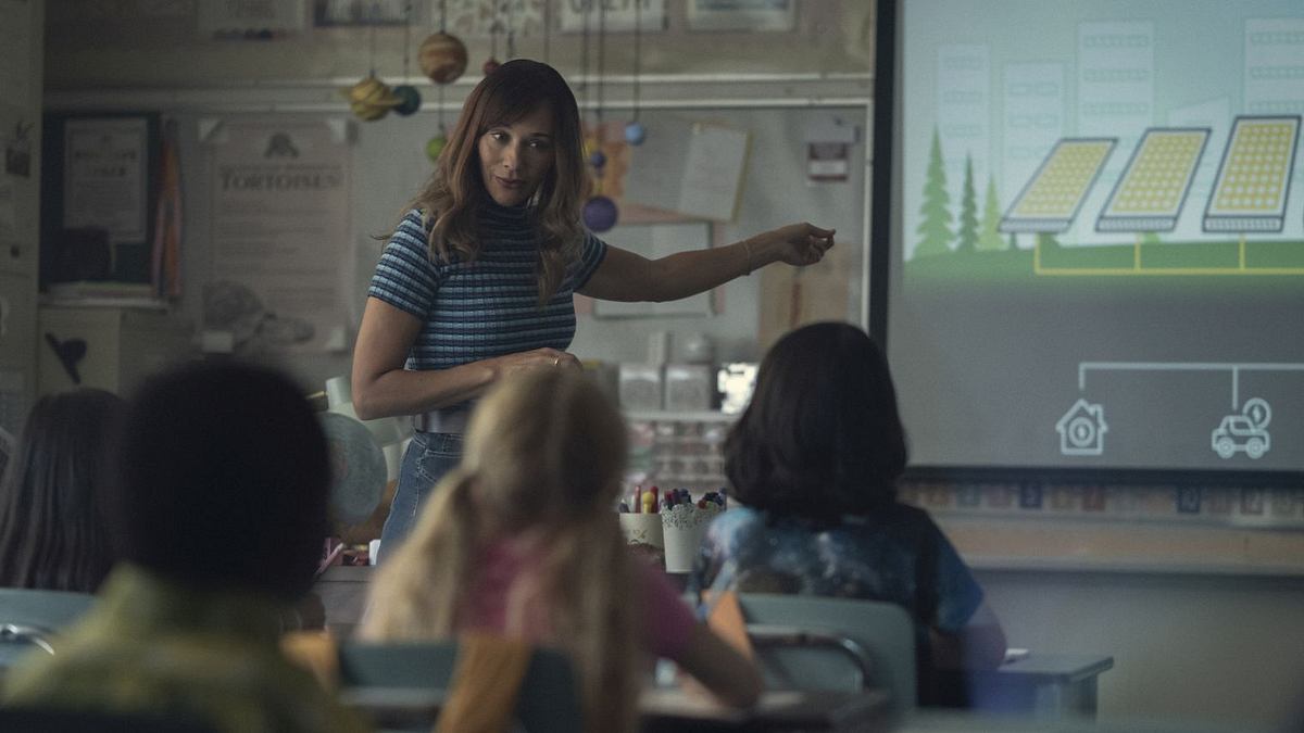 Rashida Jones als Anna in „Black Mirror: Gewöhnliche Leute“. Sie steht vor ihrer Schulklasse und deutet auf eine Leinwand.