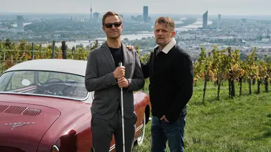 Philipp Hochmair und Andreas Guenther in „Blind ermittelt: Tod im Weinberg“ vor einem Oldtimer in den Wiener Weinbergen - Foto: ORF/Mona Film/Tivoli Film/Philipp Brozsek