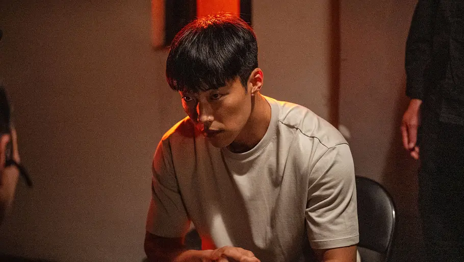 Bloodhounds Staffel 3 Geon-woo sitzt im weißen Shirt auf einem Stuhl in Bloodhounds und schaut ernst nach vorne.
