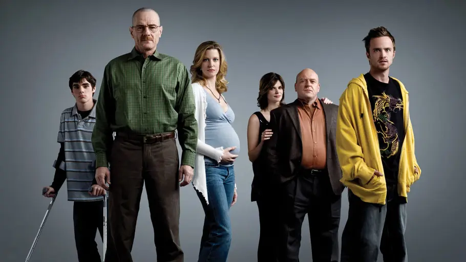 Sechs Mitglieder des „Breaking Bad“-Casts stehen vor grauem Hintergrund, darunter RJ Mitte links mit Gehstützen.
