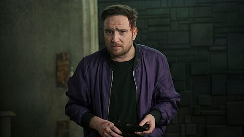 Frederick Lau steht in einer lila Bomberjacke mit einem schwarzen Shirt in einem dunklen Raum. Hinter ist eine Anthrazit-farbende Mauer. - Foto: Sasha Ostrov / Netflix