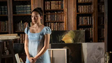 Sophie steht vor einem Bücherregal und mehreren Gemälden. - Foto: LIAM DANIEL/NETFLIX Sophie steht vor einem Bücherregal und mehreren Gemälden. - Foto: LIAM DANIEL/NETFLIX