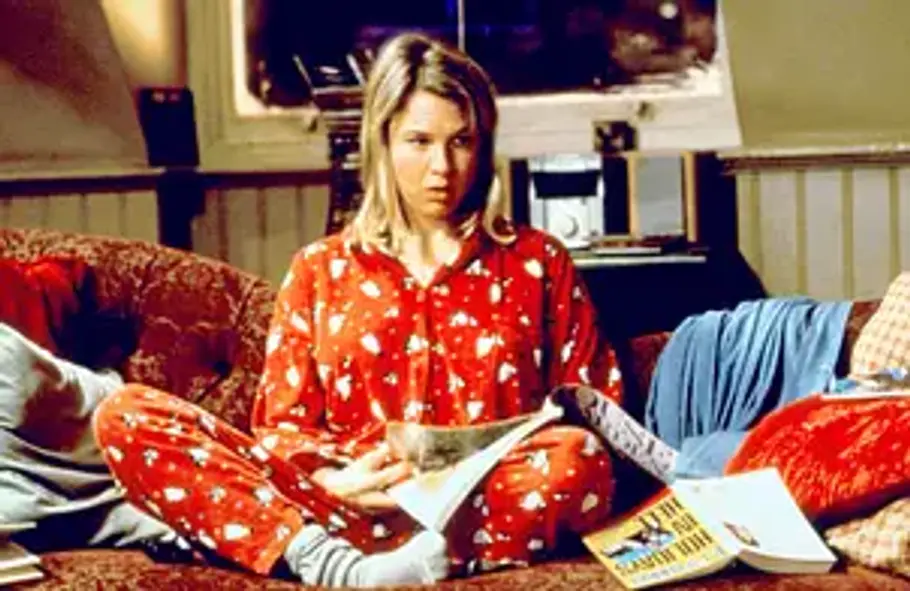 Bridget Jones Eine blonde Frau (Bridget Jones) sitzt mit einem roten Weihnachts-Pyjama auf der Couch und liest eine Zeitung.